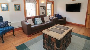 A living room with a brown leather sofa, a blue armchair, a wooden coffee table, and a television mounted on the wall.