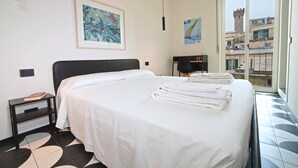 A hotel room with a large bed, a nightstand, a painting on the wall, and a window with a view of buildings.