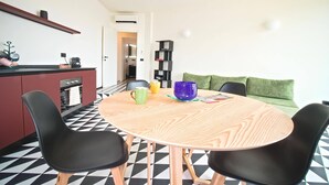 A modern kitchen with a black and white checkered floor, a round wooden table with black chairs, and a green sofa in the background.