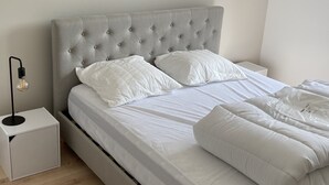 A neatly made bed with a tufted headboard, white bedding, and a bedside lamp. - Gîte la Margotine (Saint-Quentin-la-Motte-Croix-au-Bailly)