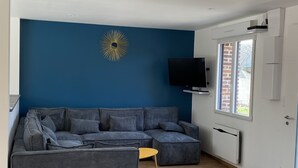 A modern living room with a sectional sofa, a flat-screen TV, and a decorative sunburst wall piece. - Gîte la Margotine (Saint-Quentin-la-Motte-Croix-au-Bailly)
