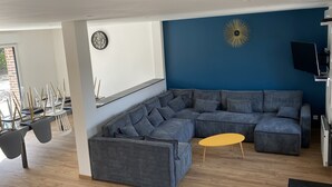 A modern living room with a sectional sofa, a yellow coffee table, and a blue accent wall. - Gîte la Margotine (Saint-Quentin-la-Motte-Croix-au-Bailly)