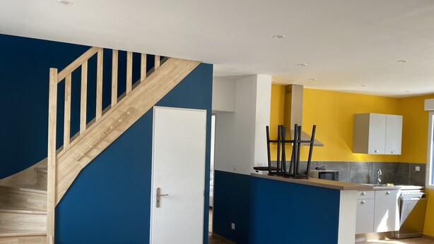 A modern kitchen with a wooden staircase, a white door, and a yellow accent wall. - Gîte la Margotine (Saint-Quentin-la-Motte-Croix-au-Bailly)
