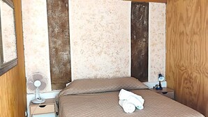 Een slaapkamer met een bed, nachtkastje, spiegel en plafondventilator.