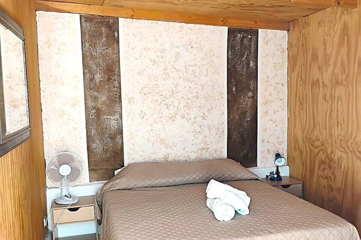 Quarto com cama, mesa de cabeceira, espelho e ventilador de teto.