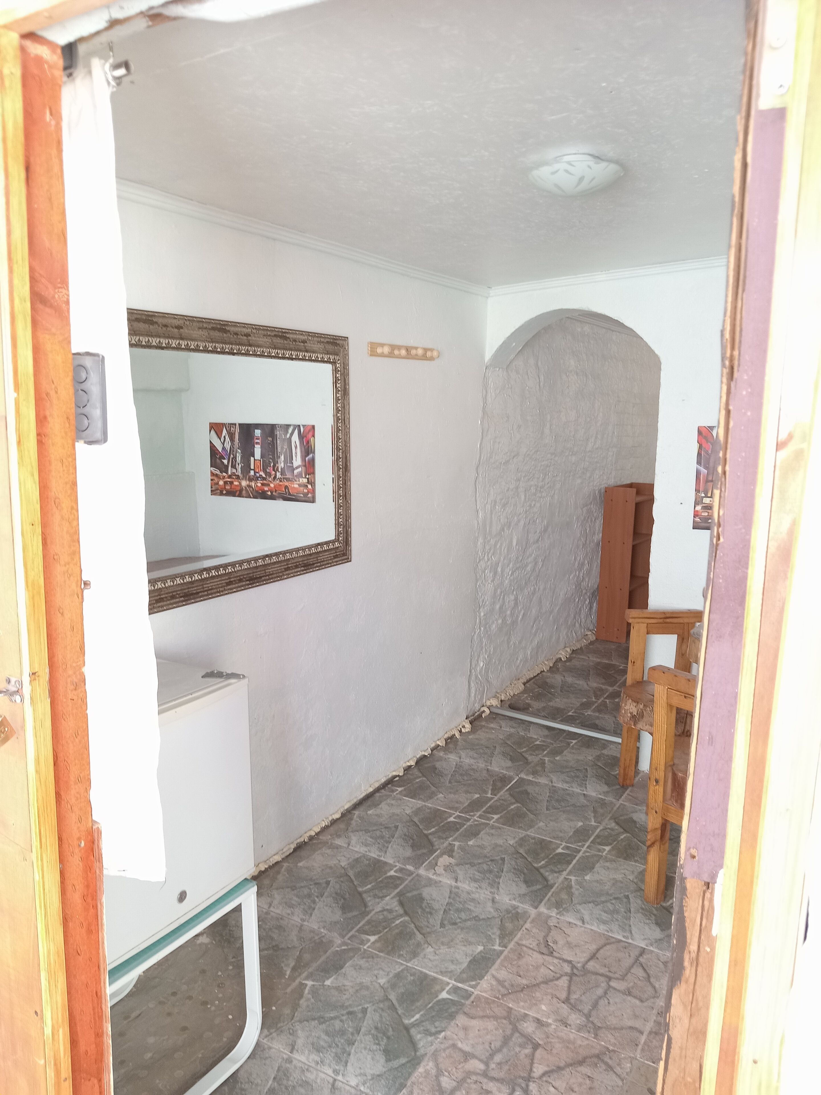 A hallway with a white wall, a framed picture, a wooden chair, and a tiled floor.