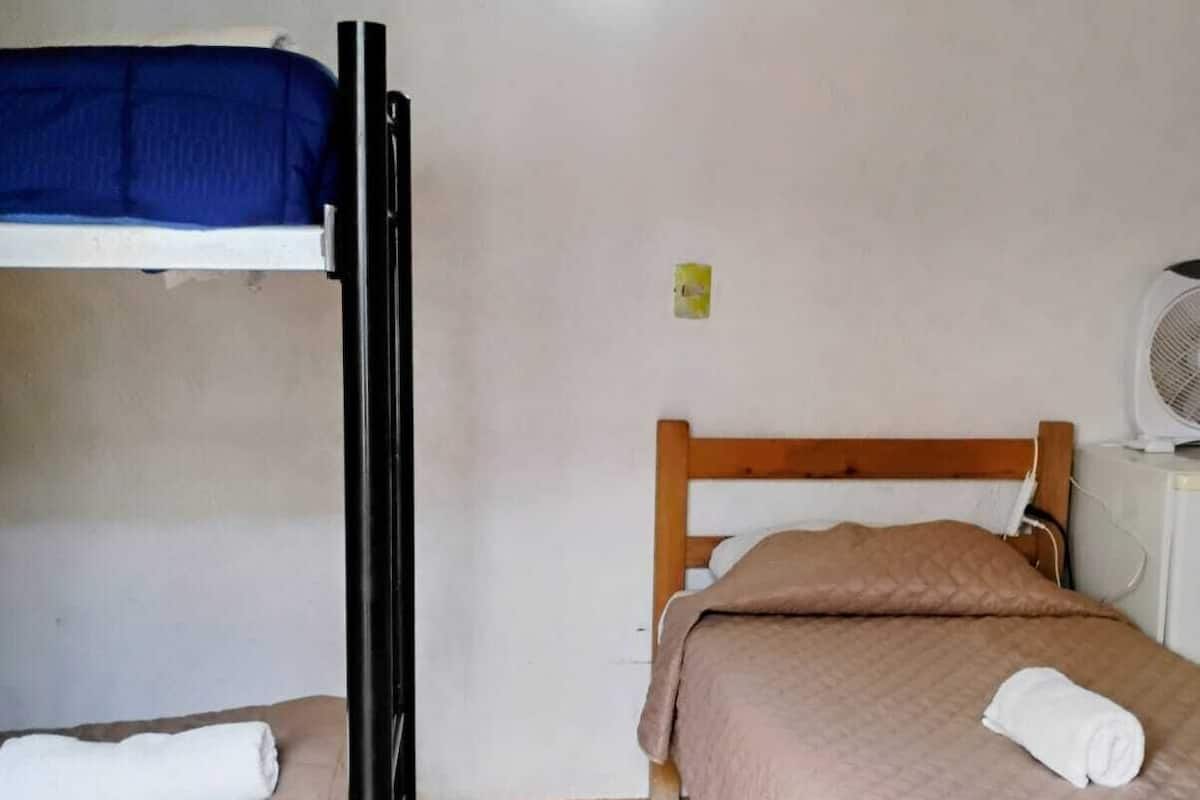 Quarto com uma cama de solteiro, uma beliche, um aquecedor e um ventilador.