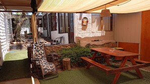 Een buitenterrein met terras, een houten tafel en stoelen, een hanglamp en een op de muur bevestigd bord met een biertje erop.