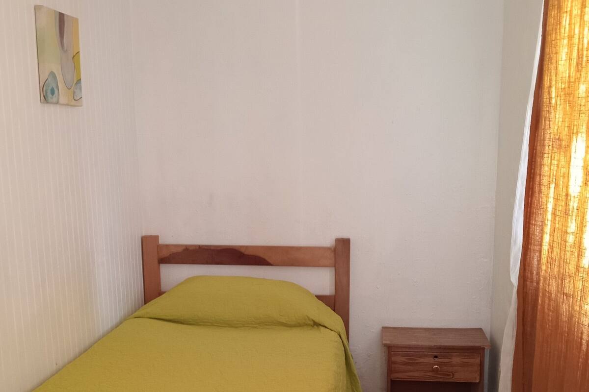 Quarto pequeno com uma cama de solteiro, cabeceira de madeira, mesa de cabeceira e um armário pequeno.