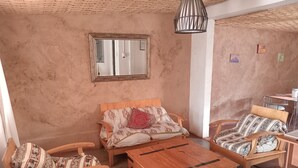 Een gezellige kamer met een houten bank, twee houten stoelen, een houten bijzettafeltje en een klein tafeltje met een stoel.