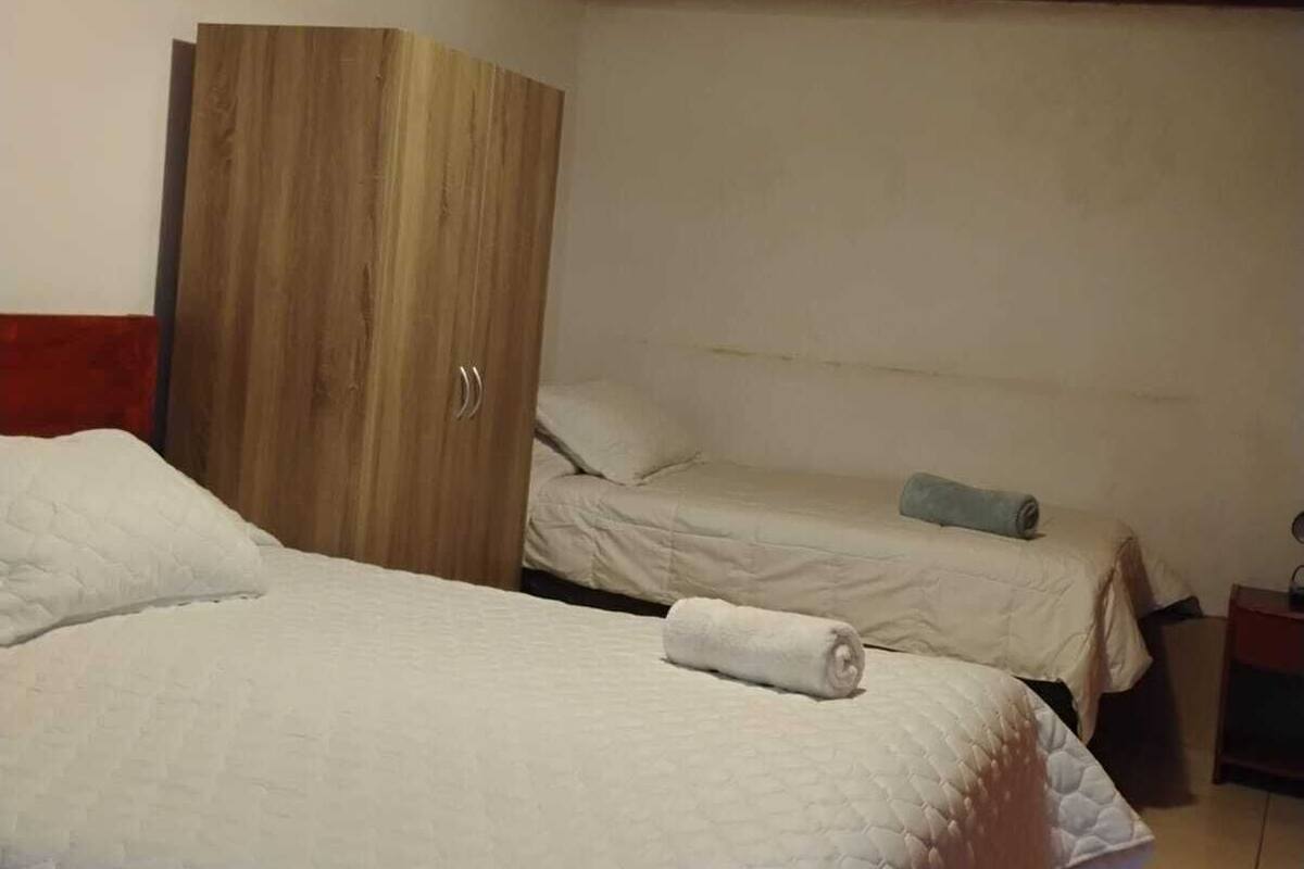 Quarto com duas camas, um guarda-roupa de madeira e uma luminária no teto.