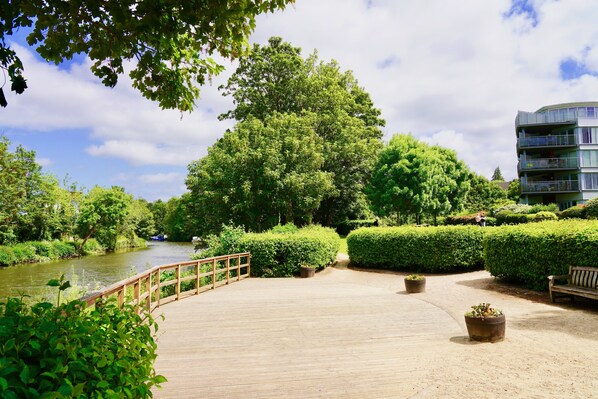 Stroll along the boardwalk to the serene river, surrounded by lush greenery and a well-maintained hedge.