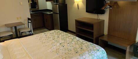 A hotel room with a bed, a desk, a chair, a TV, a microwave, a refrigerator, and a wooden wardrobe.