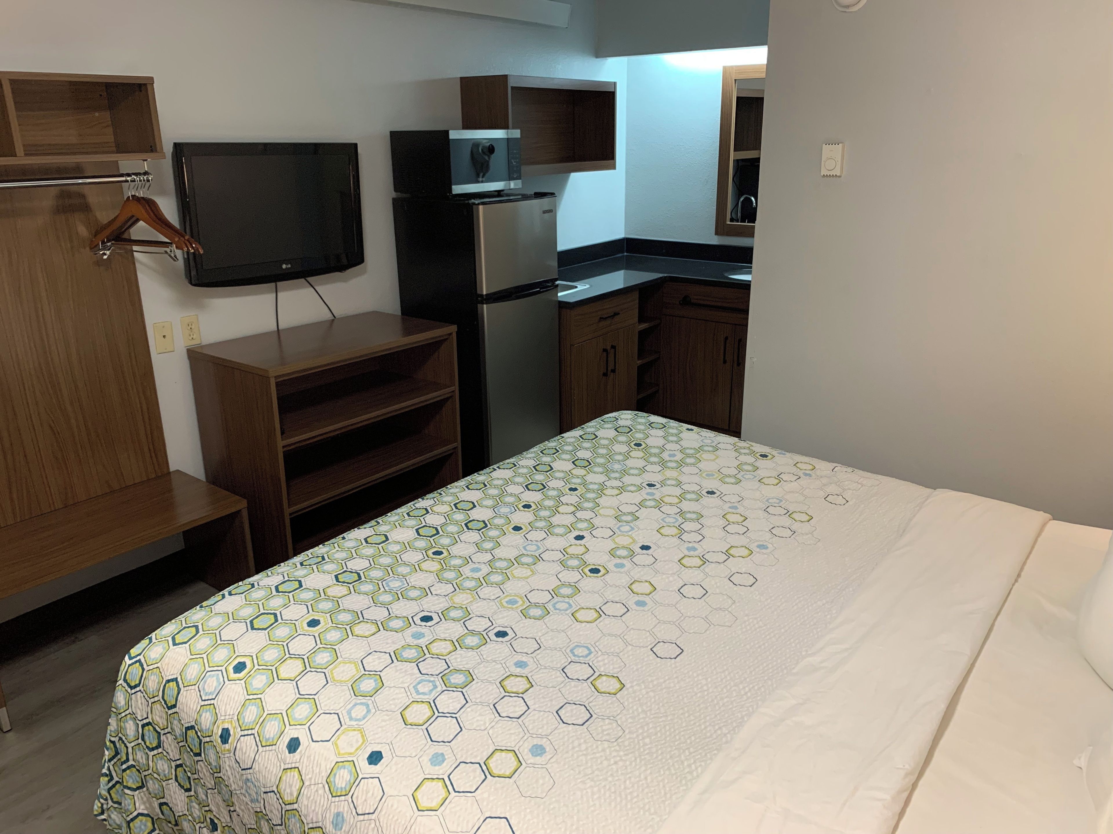 A hotel room with a bed, a television, a microwave, a refrigerator, and wooden cabinets.