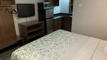A hotel room with a bed, a television, a microwave, a refrigerator, and wooden cabinets.