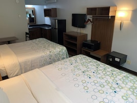 Habitación de hotel con dos camas, televisor, microondas y una pequeña kitchenette.