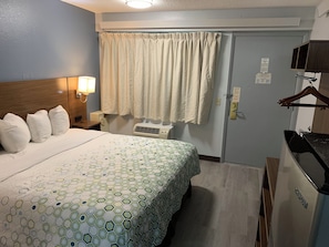 Une chambre d’hôtel comprenant un lit, une lampe de chevet, une fenêtre avec des rideaux, un porte-manteau et un mini-bar.