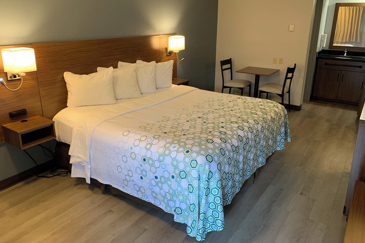 A hotel room with a neatly made bed, bedside tables, a desk, and a chair.