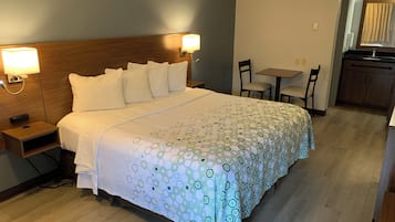 Una habitación de hotel con cama, lámparas de noche, una mesita, sillas y una kitchenette.