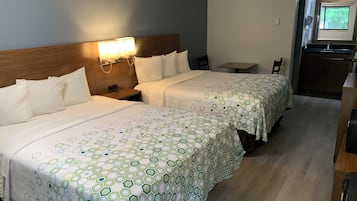 A hotel room with two beds, a small table, a chair, and a kitchenette area.