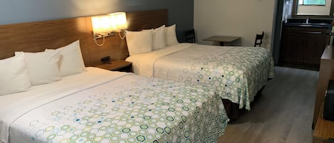 Habitación de hotel con dos camas, una mesita, una silla y un área de kitchenette.