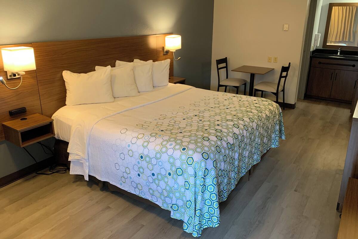 Een hotelkamer met een net opgemaakt bed, nachtkastjes, een bureau en een stoel.