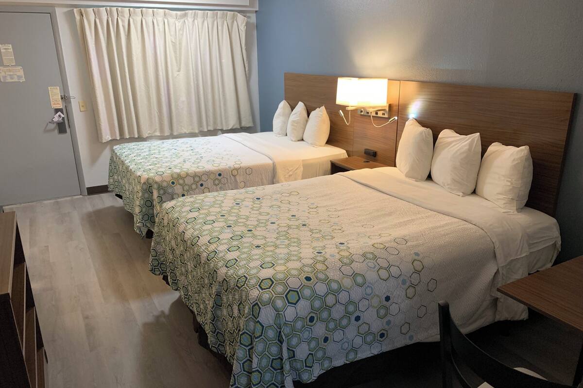 Een hotelkamer met twee bedden, elk met een sprei met een honingraatpatroon, een houten hoofdbord, een bedlampje en een klein tafeltje.