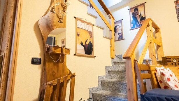 A staircase with wooden railings and a mirror, a bed with a floral pillow, and a wall-mounted light switch. - [Apartment in the Charming Courtyard] Lake Lugano (Brusimpiano)