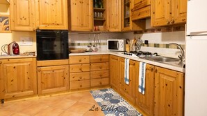 A kitchen with wooden cabinets, a stove, a microwave, and a sink. - [Apartment in the Charming Courtyard] Lake Lugano (Brusimpiano)