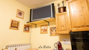 A kitchen with wooden cabinets, a black refrigerator, a microwave, and a television mounted on the wall. - [Apartment in the Charming Courtyard] Lake Lugano (Brusimpiano)