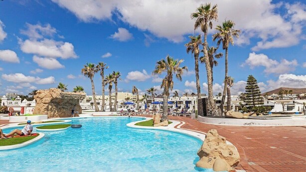 Una piscina con palmeras, una formación rocosa y una montaña al fondo.
