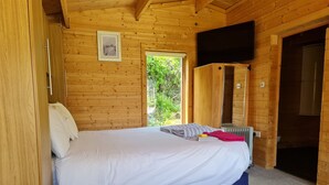 A wooden cabin room with a bed, a television, and a window.