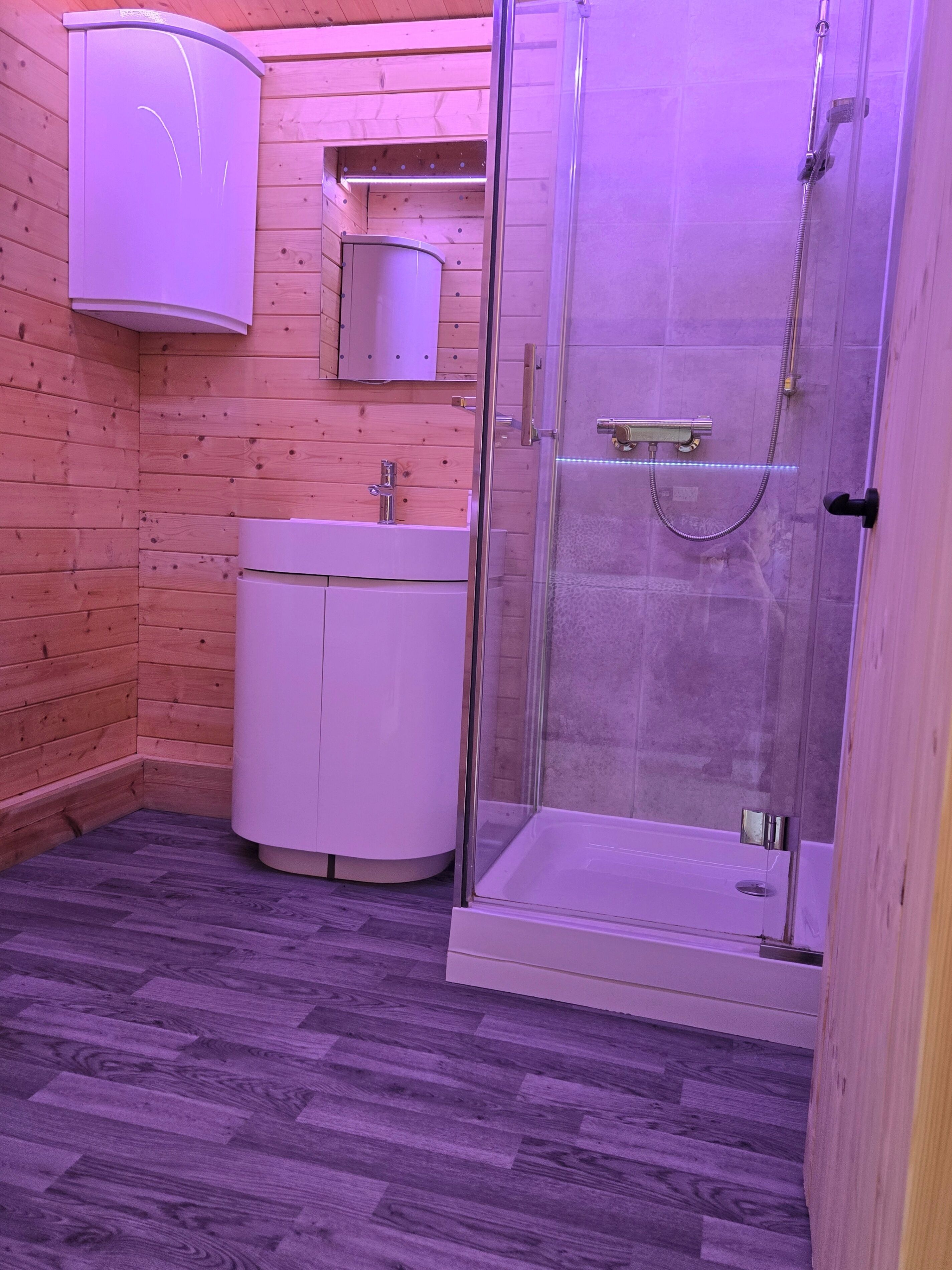 A bathroom with wooden walls, a white sink, and a glass-enclosed shower.