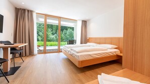 A modern bedroom with a wooden bed, a desk, and a view of greenery through a glass door. - 192A Greva Apartments 2 (Santa Cristina Valgardena)