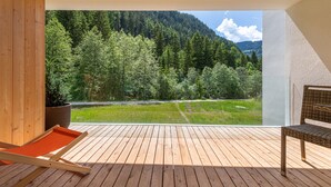 Una terraza de madera con vistas a una montaña boscosa y un río.