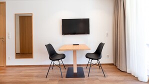 Una habitación moderna con una mesa de madera, dos sillas negras, un televisor de pantalla plana en la pared y una puerta de madera.