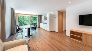 Een moderne woonkamer met een eetgedeelte, een keuken en een aan de muur bevestigde televisie.