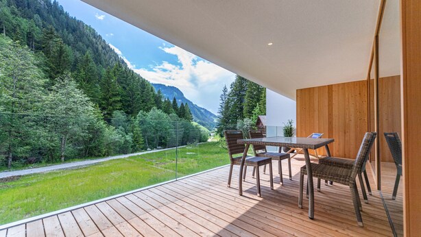 Een houten terras met een tafel en stoelen met uitzicht op een bergachtig landschap.