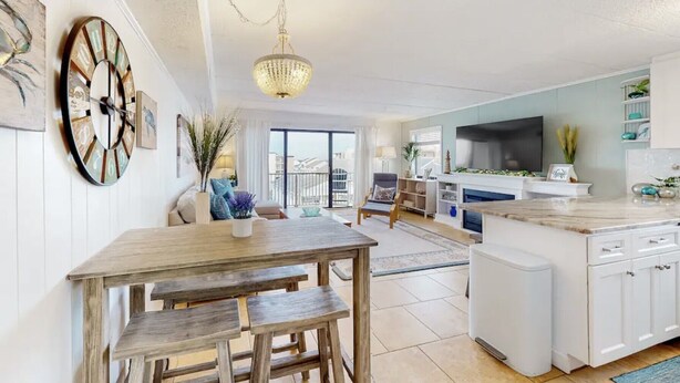 Eine moderne Küche mit einer zentralen Kochinsel, ein Essbereich mit Holztisch und ein Wohnzimmer mit Sofa und Fernseher.