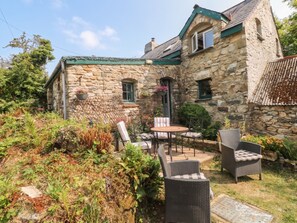 A stone house with a garden patio featuring wicker furniture and a small table. - Penfeidr Newydd (Newport)