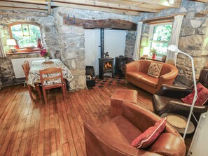 A cozy room with a stone wall, a fireplace, a dining table with chairs, a leather sofa, and a lamp. - Penfeidr Newydd (Newport)