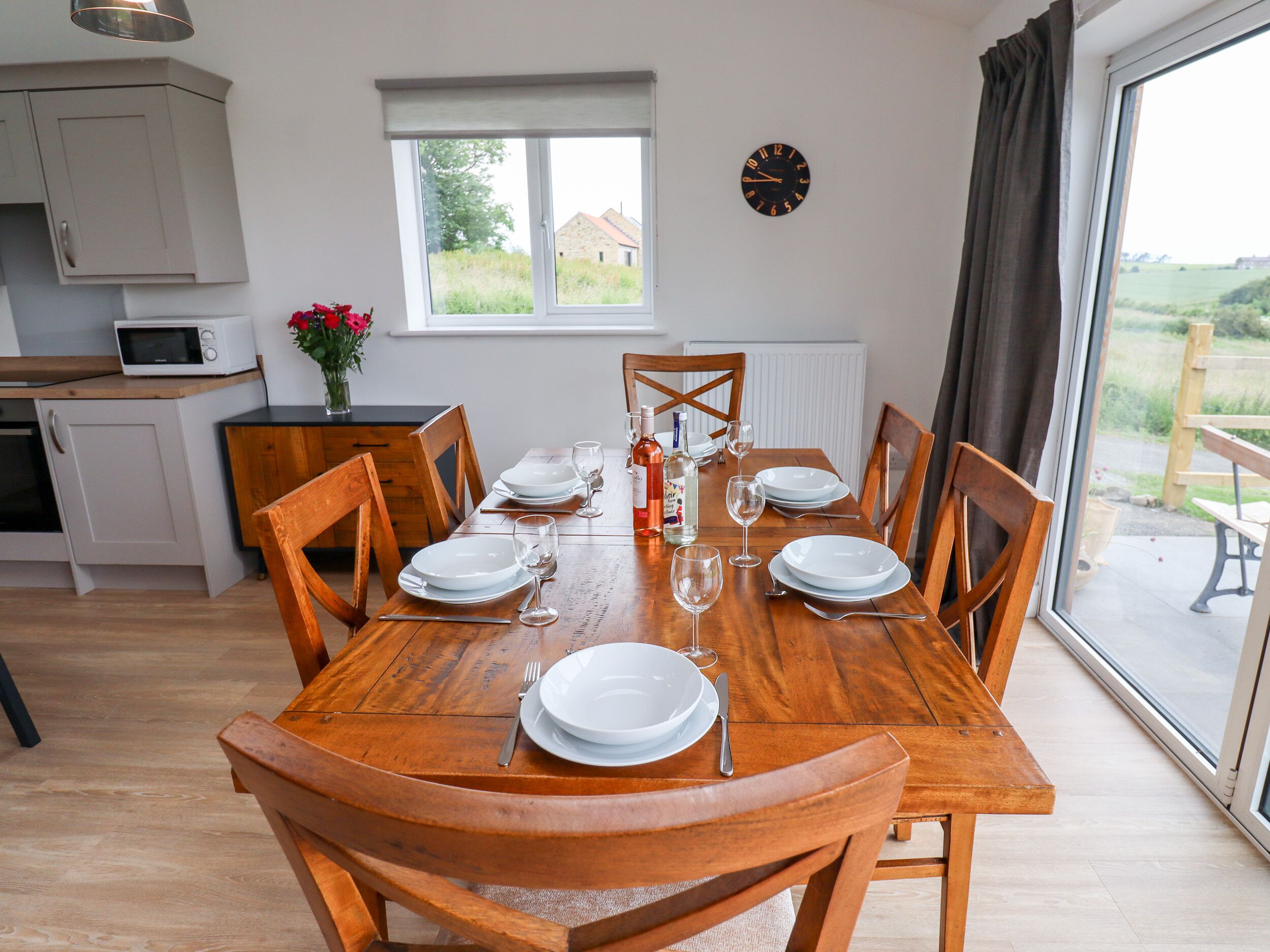 Un coin repas avec une table en bois dressée pour six personnes, entourée de chaises en bois. Une fenêtre offre une vue sur l’extérieur.
