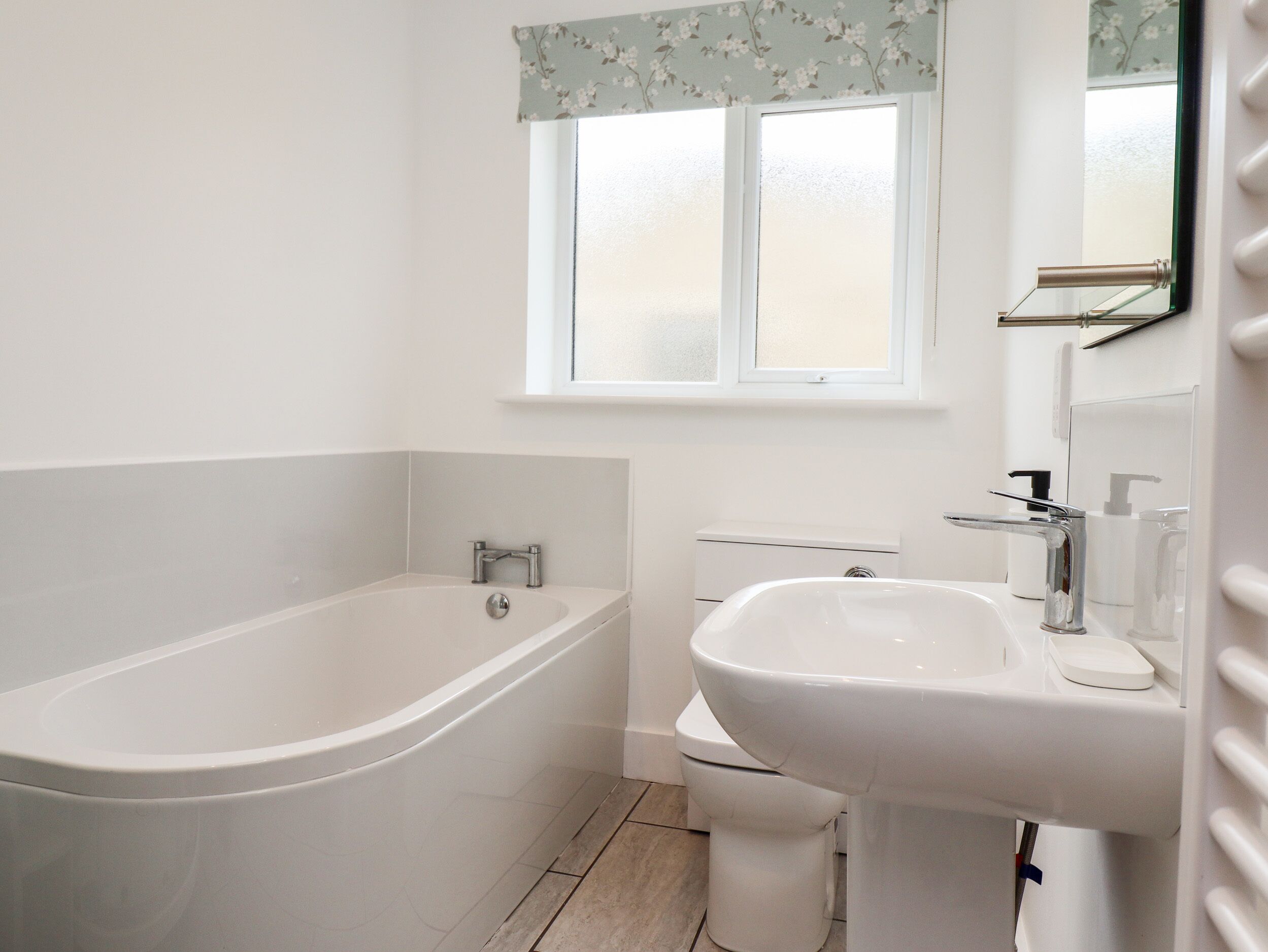 A bathroom with a bathtub, toilet, sink, and a window with floral curtains.