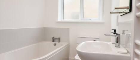 A bathroom with a bathtub, toilet, sink, and a window with floral curtains.