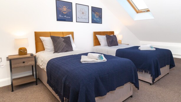 Une chambre avec deux lits, une table de chevet et une lucarne.