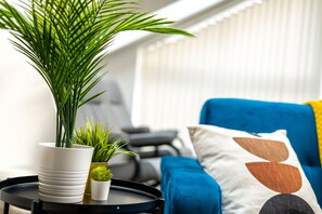 A living room with a blue sofa, a white potted plant, and a small table with a tray. - St Mary's Apartment (Huntingdon)