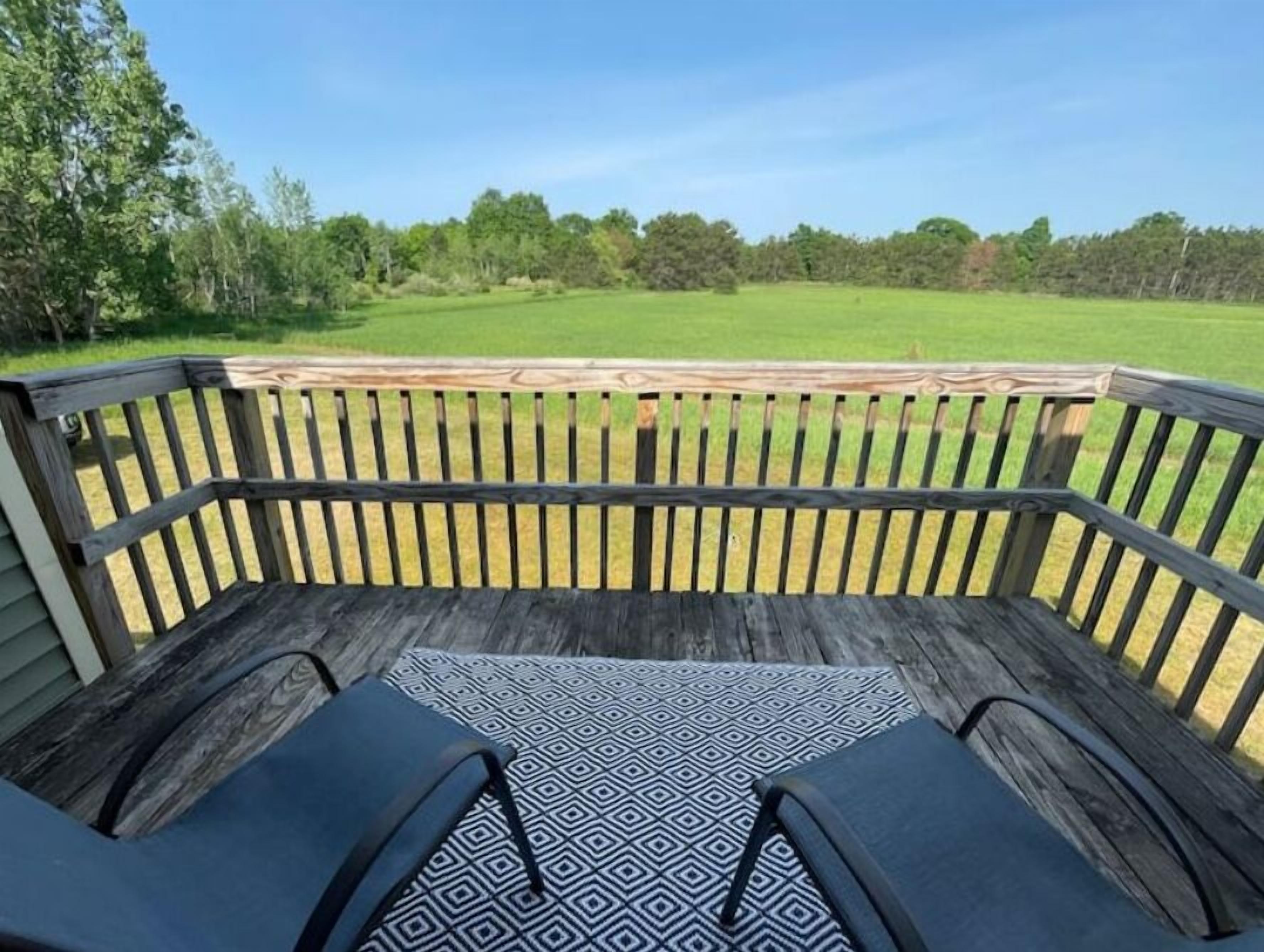 A wooden deck with a patterned rug, a bench, and a view of a green field and trees.