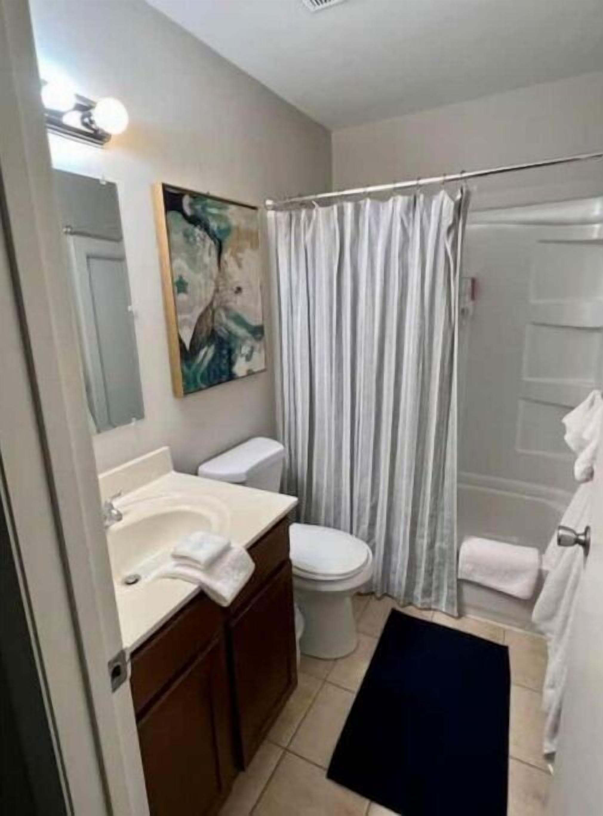 A bathroom with a toilet, sink, and mirror. There is a shower curtain and a towel rack.