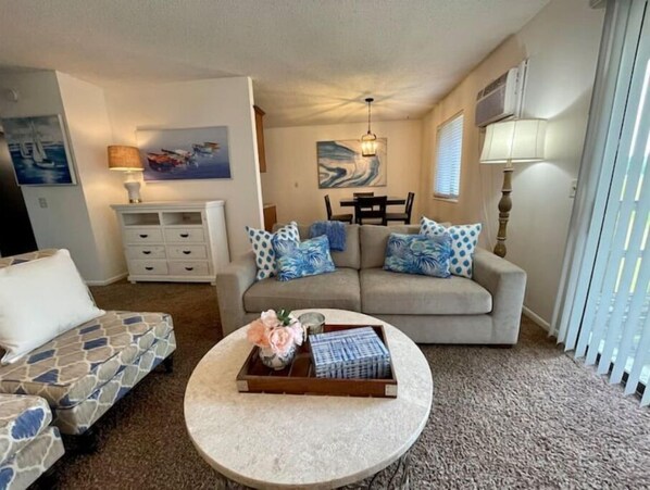 A living room with a sofa, a round coffee table with a tray of items, a white cabinet, and a painting on the wall.