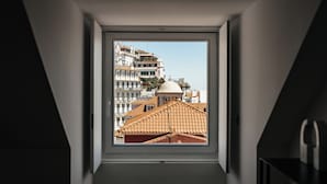 Uitzicht vanuit een raam in een kamer met schuine wanden, op een stadsgezicht met gebouwen en een koepelstructuur.